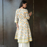 Woman wearing a floral kurta with white pants against a dark wall.