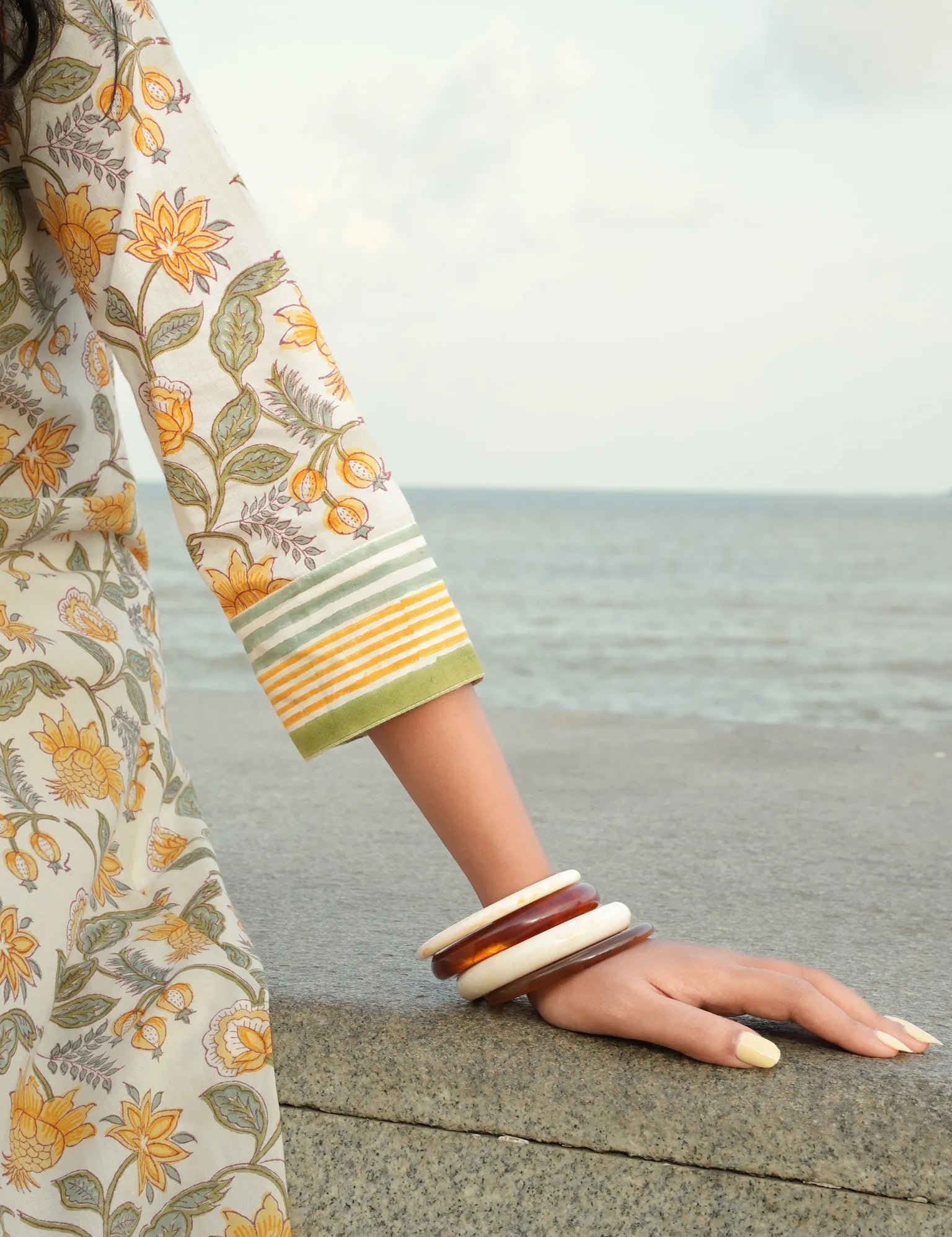 Person wearing a floral dress and bangles by the sea