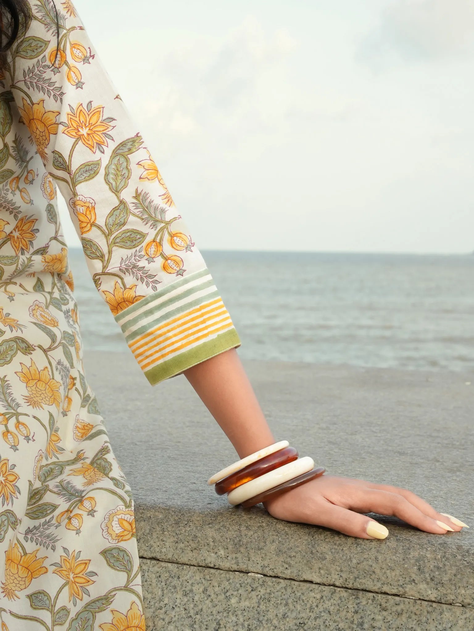 Person wearing a floral dress and bangles by the sea