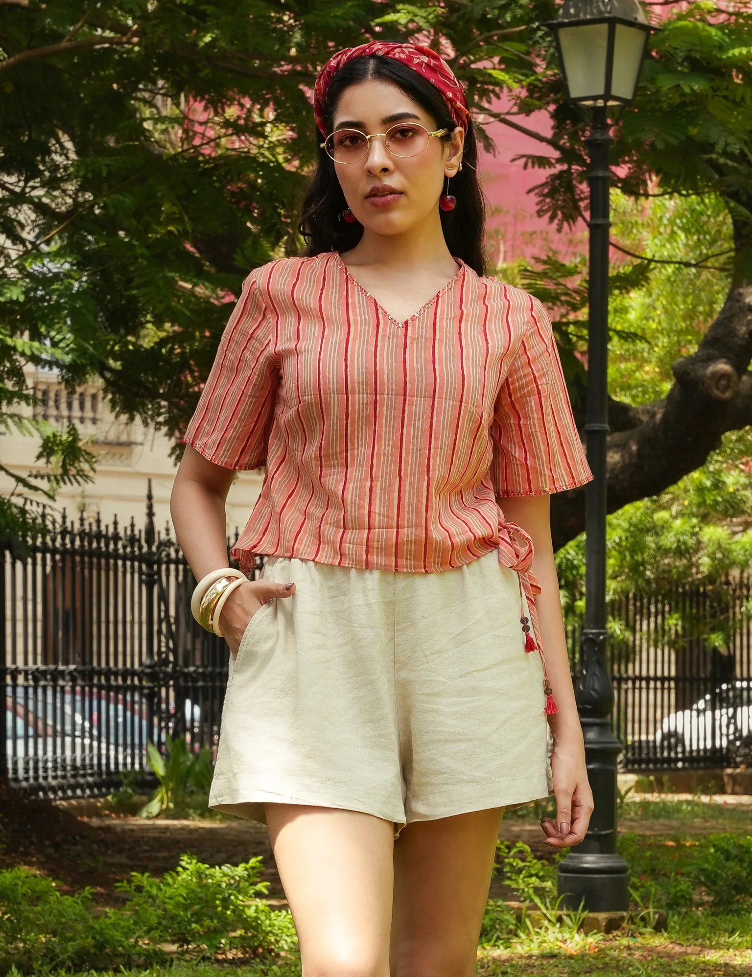 Woman wearing a red and white striped top and beige shorts in a park setting.