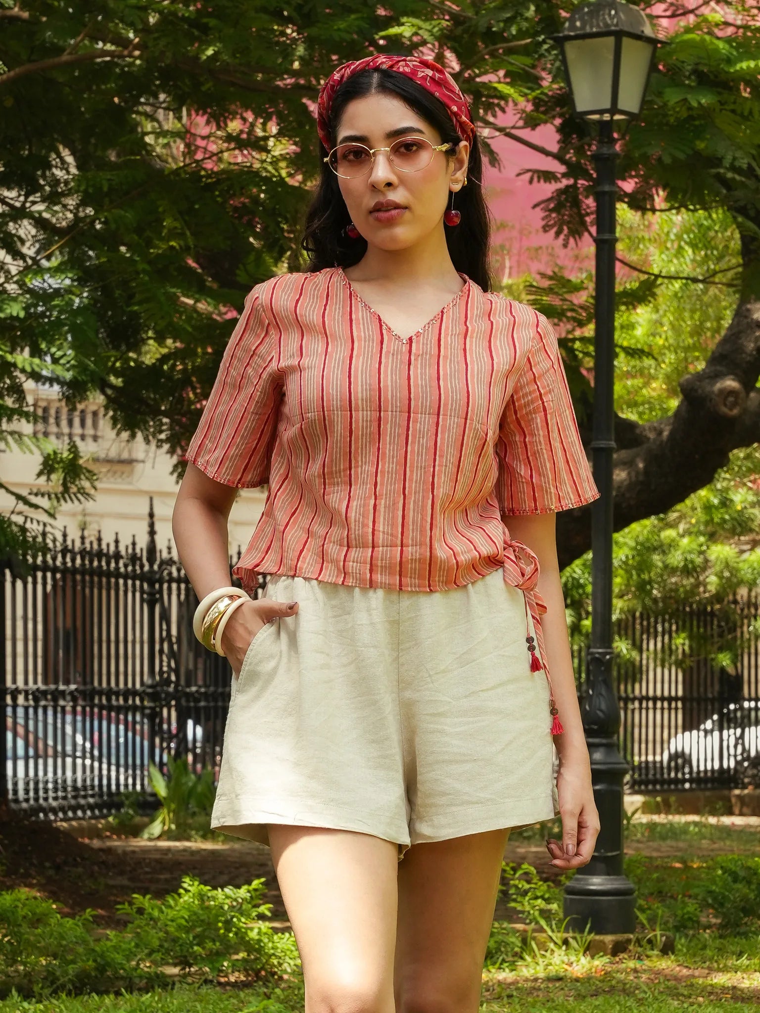 Woman wearing a red and white striped top and beige shorts in a park setting.