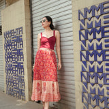 Woman in a red top and patterned skirt standing against a textured wall with geometric designs.
