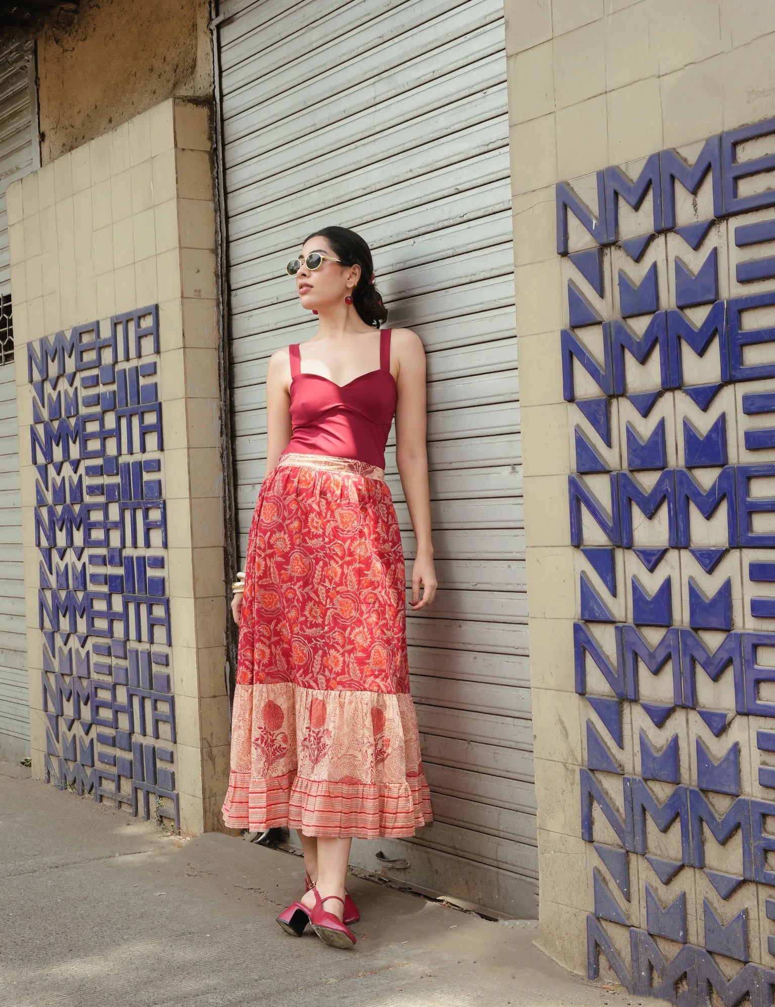 Woman in a red top and patterned skirt standing against a textured wall with geometric designs.