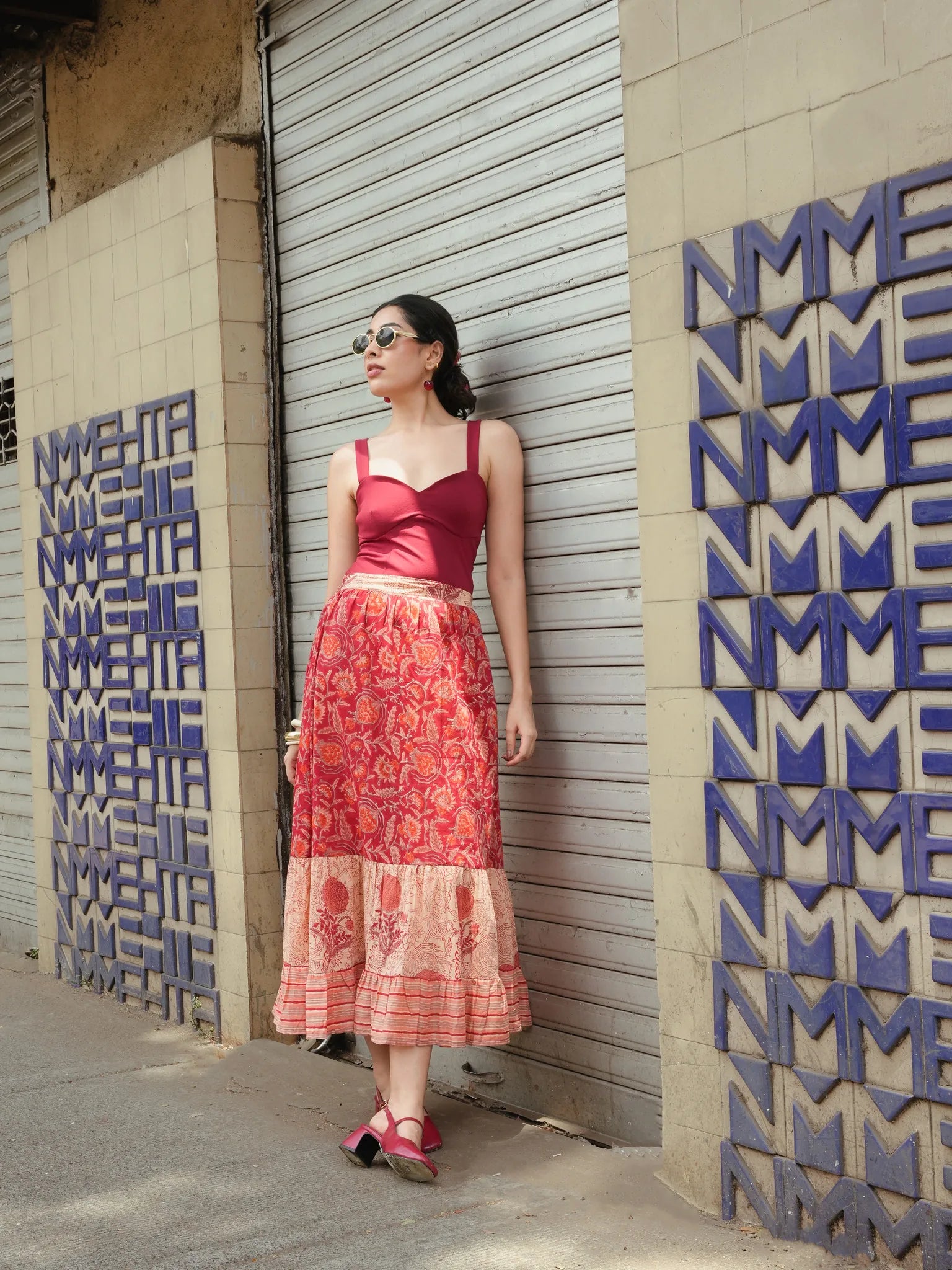 Woman in a red top and patterned skirt standing against a textured wall with geometric designs.