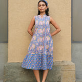 Woman wearing a blue floral dress standing against a beige wall.