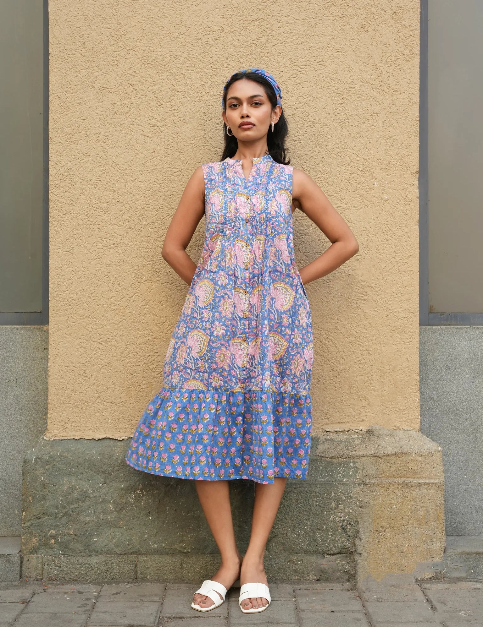 Woman wearing a blue floral dress standing against a beige wall.
