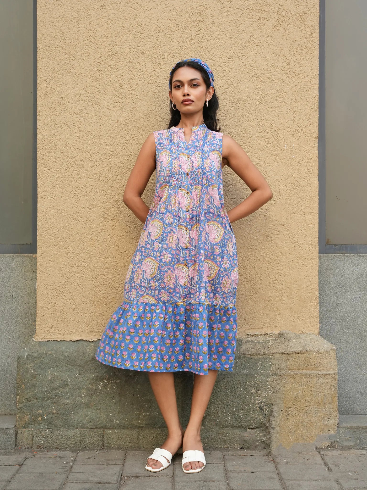 Woman wearing a blue floral dress standing against a beige wall.
