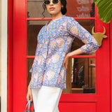 Woman wearing a blue floral blouse and white pants standing in front of a red door.