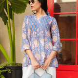 Woman wearing a blue patterned top holding a light blue handbag in front of a red door.