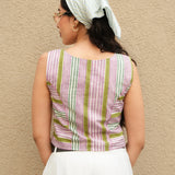Woman wearing a striped sleeveless top and white pants against a beige wall.