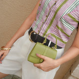 Person holding a green handbag with a striped shirt and white shorts against a beige wall.