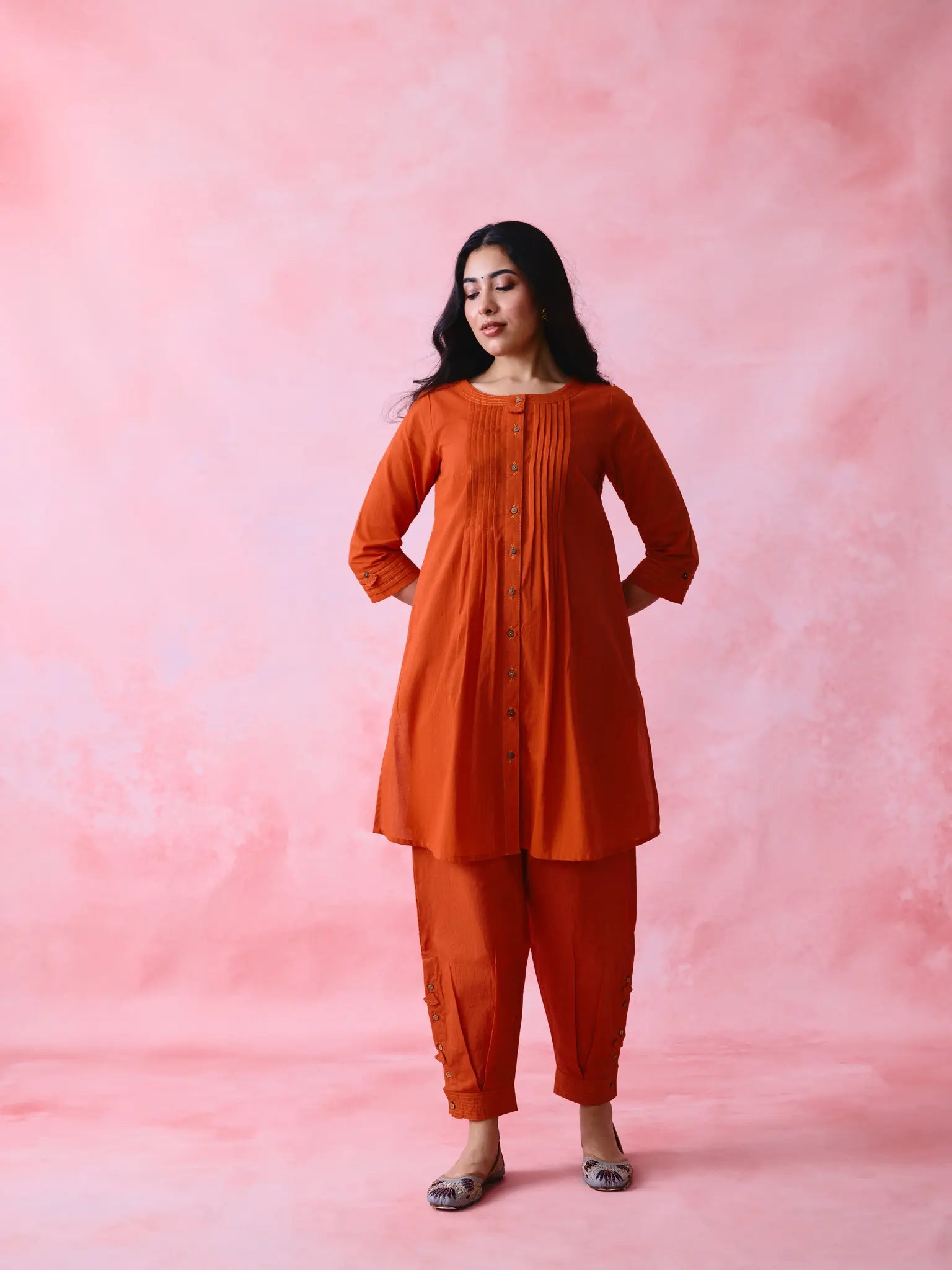 Red cotton Mangalgiri co-ord with a front-pleated, contrast-stitched kurta and button-and-cotton-bell pant hems.
